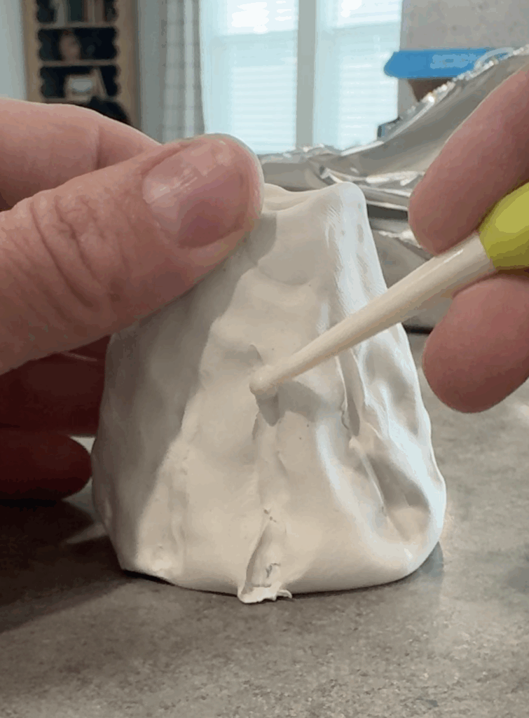 Close-up of sculpting tool adding folds and texture to a clay ghost candlestick holder.