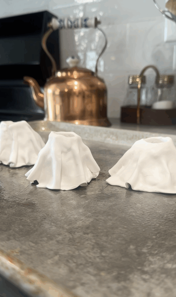 Unbaked clay ghost candlestick holders lined up on a baking tray, ready for the oven.
