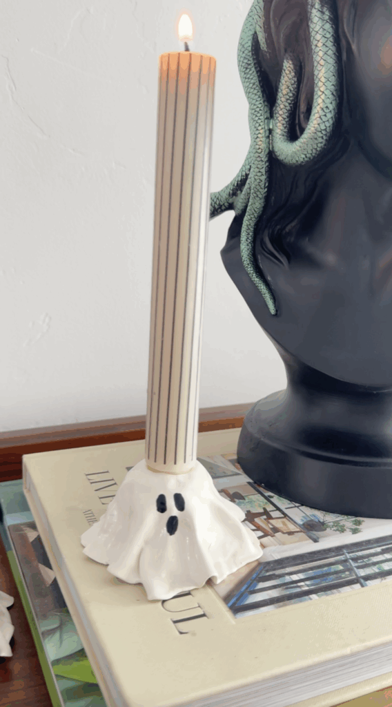 Ghost candlestick holder with a striped taper candle displayed on stacked books for Halloween décor.