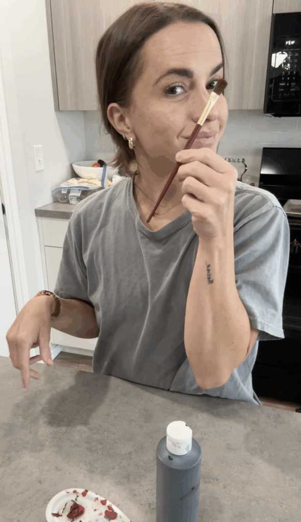 Woman smiling while holding a paintbrush during ghost candlestick holder DIY project.