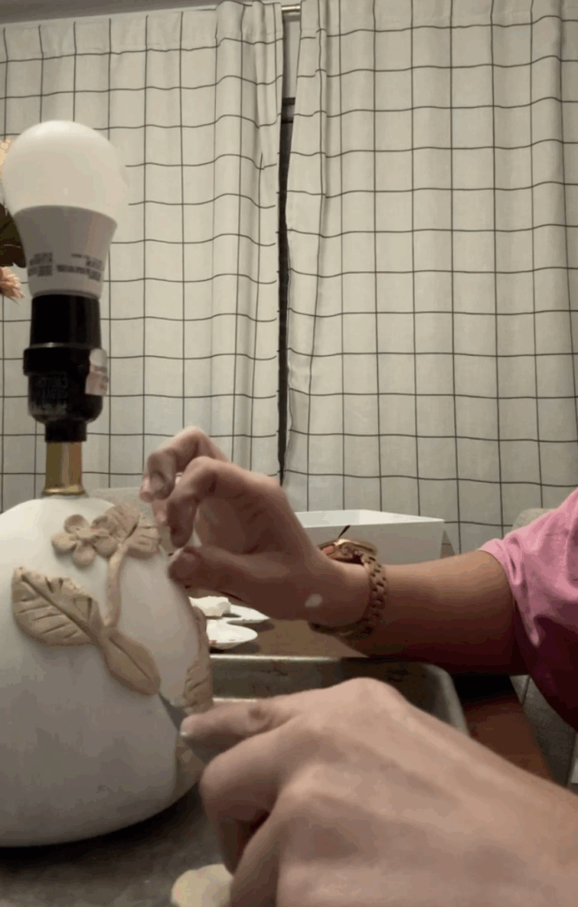 Attaching clay leaves and flowers by hand to the base of a lamp before painting in a DIY makeover.