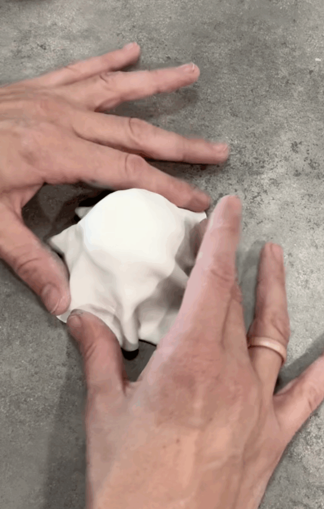 Hands draping white polymer clay over a foil form to create the base of a ghost candlestick holder.