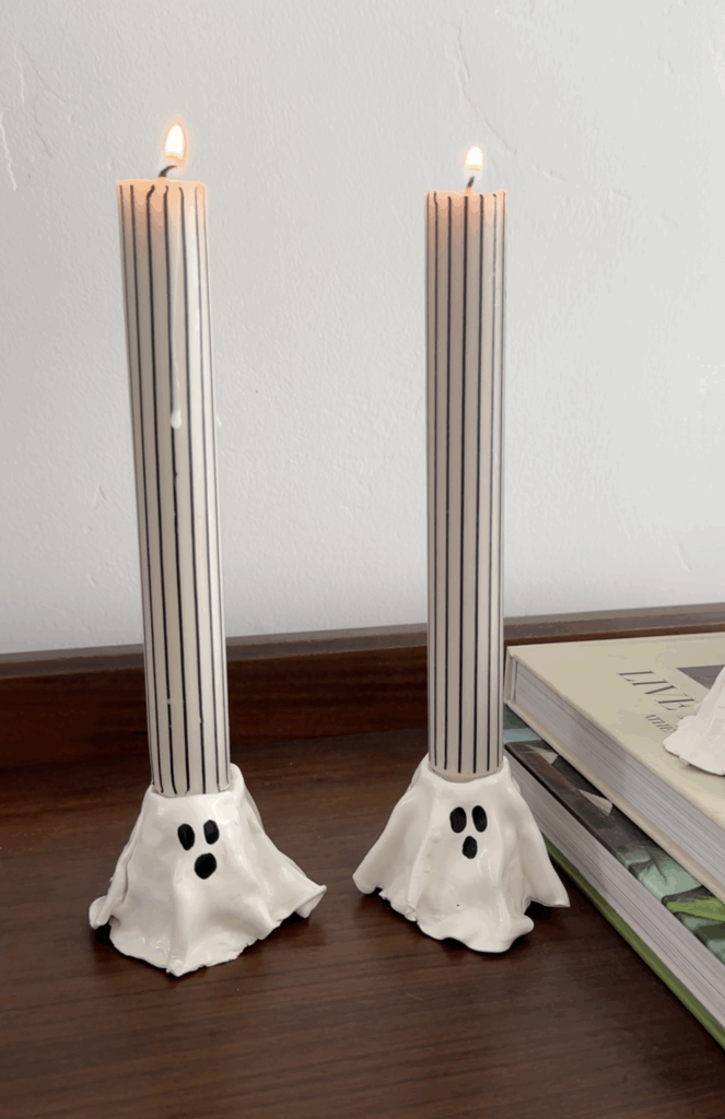 Two DIY ghost candlestick holders with tall striped taper candles lit on a table.