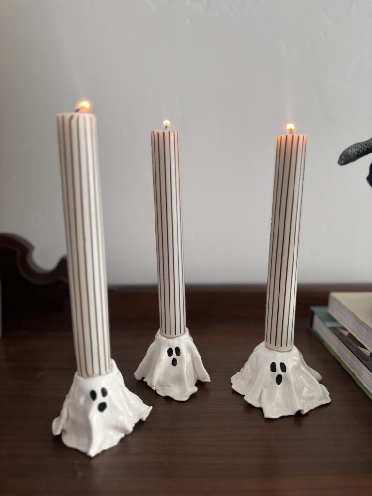 Handmade ghost candlestick holders with striped taper candles glowing on a wooden table.