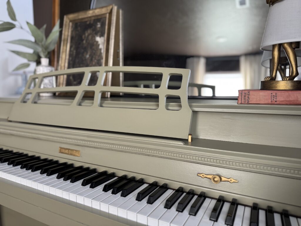 Close-up of painted green piano keys and hardware with vintage books and gold rabbit lamp decor.