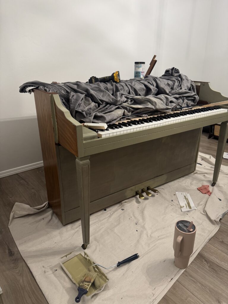 Piano half painted with green paint, surrounded by tools and drop cloth during makeover.