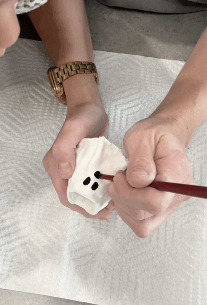 Close-up of painting black eyes and mouth on a clay ghost candlestick holder.