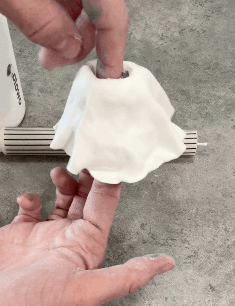 Hands shaping the opening of a clay ghost candlestick holder to fit a taper candle.